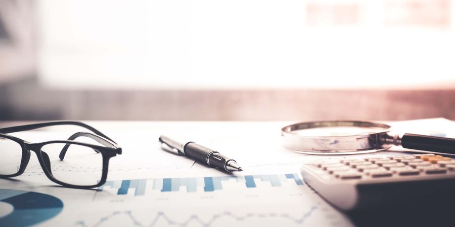 Foto von Stift, Brille, Block, Taschenrechner und Lupe auf einem Schreibtisch | Herausforderungen im Projekt