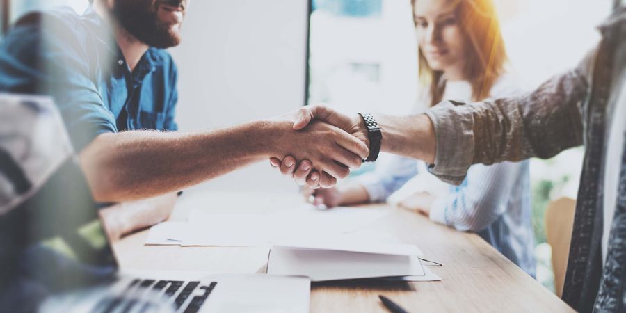 Foto zwei Menschen, die über einen Tisch Hände schütteln | Kundenorientierung & Geschäftsprozesse