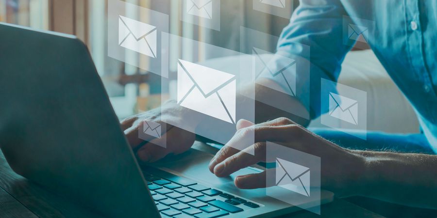 Foto von Person vor Laptop mit E-Mail Icons in der Luft schwebend | Newsletter
