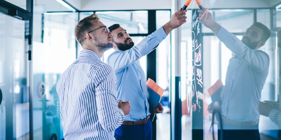 Foto von 2 Männern, die an einem transparenten Moodboard planen | Projektmanagement + Effektive Trainingsorganisation